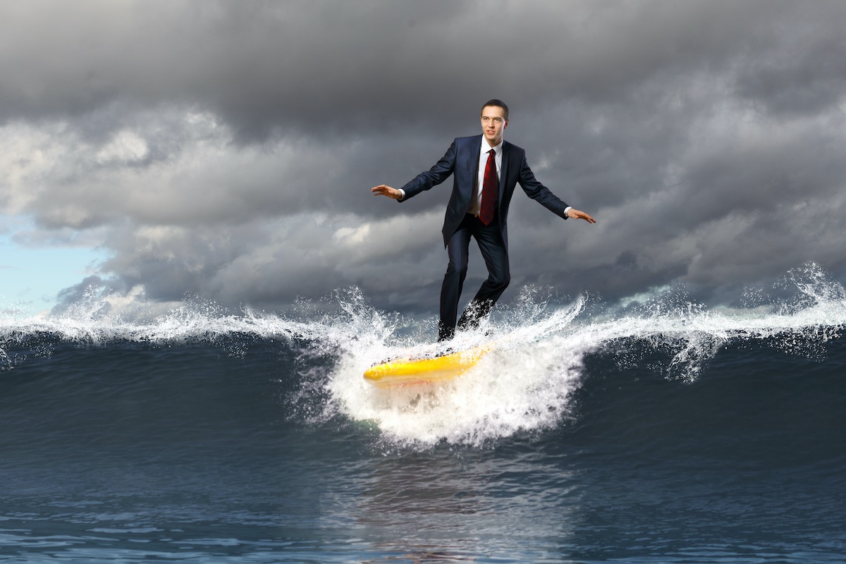 A businessman in a suit surfing an ocean wave while storm is coming