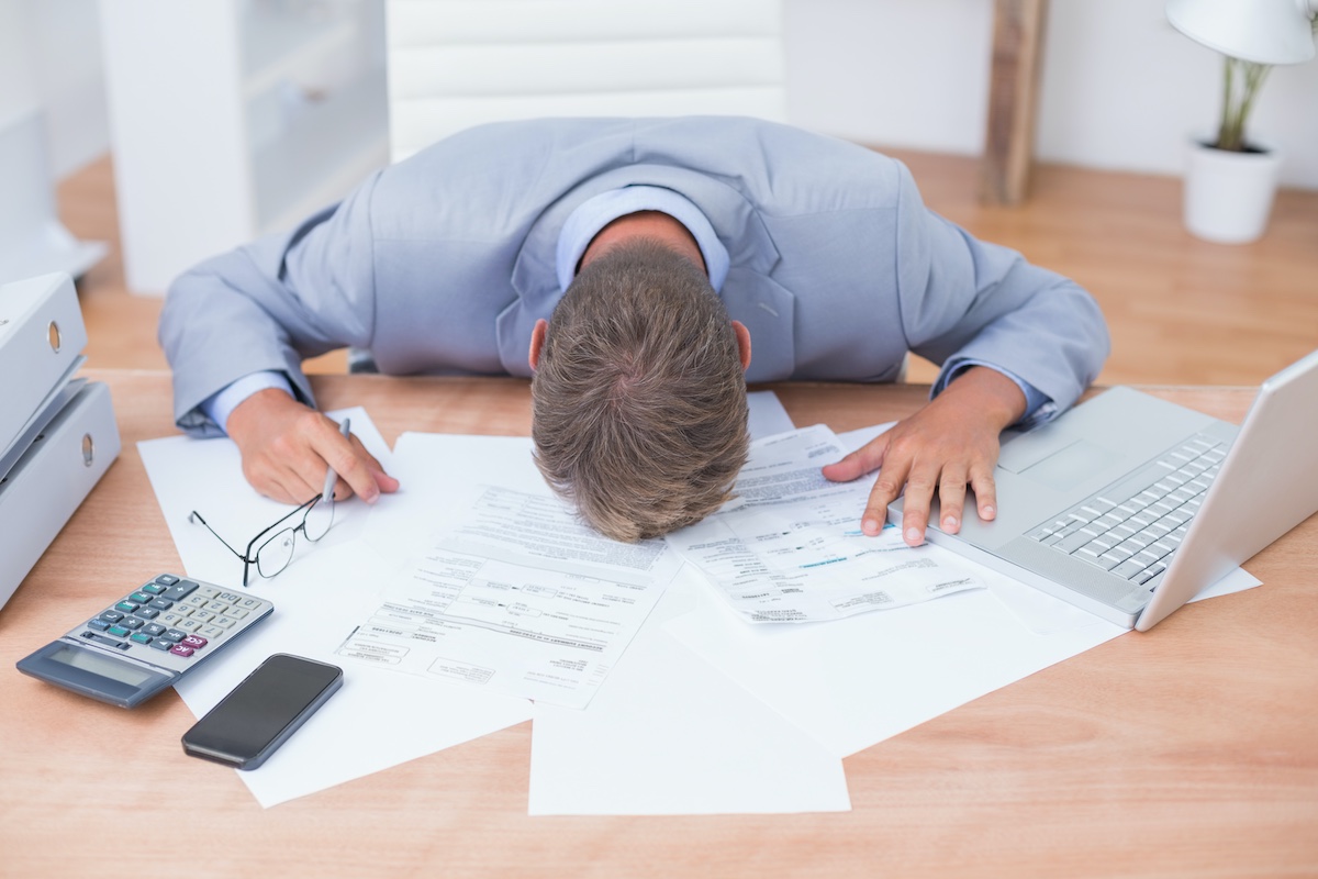 Frustrated manager lying face down on his desk covered in documents